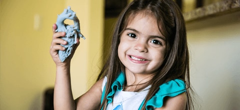 A young girl, holding a 3D printed medical model of her own heart that was used for Surgical planning 