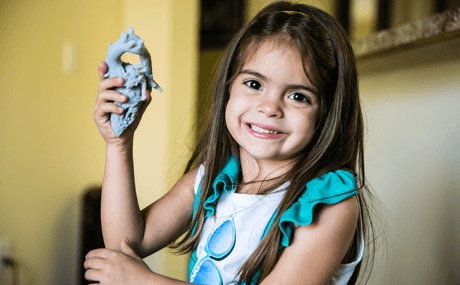 A young girl, holding a 3D printed medical model of her own heart that was used for Surgical Planning 